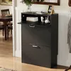 A black shoe cabinet with its top flap open, displaying books and toiletries, is placed in a hallway next to a dining area. Náhľad obrázku produktu
