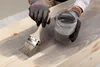 A person is applying a gray stain to a wooden surface with a brush. Voir les images du produit