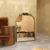 A decorative arched mirror with a floral motif is placed in a room with wooden furniture and textured walls. Podgląd zdjęcia produktu