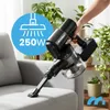 A hand holding a cordless vacuum cleaner over a sofa, with plants in the background. Podgląd zdjęcia produktu