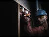 A man wearing a hard hat and safety glasses is using a cordless drill to work on a wooden frame. Náhľad obrázku produktu