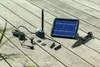A solar-powered fountain pump kit is laid out on a wooden deck. Produktbild-Vorschau