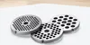 Three metal grinder plates with holes of different sizes are arranged on a white surface with a light wooden background. Anteprima dell’immagine prodotto