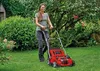 A woman is mowing her lawn with a red lawnmower in a garden. Produktbild-Vorschau