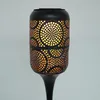 A close-up view of a black solar-powered garden light with intricate cut-out patterns that emit a warm, orange glow. Produktbild-Vorschau