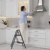 A woman is cleaning a kitchen range hood while standing on a step stool. Produktbild-Vorschau