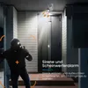 A burglar is attempting to break into a house at night, and a security camera with a siren and spotlight is activated. Produktbild-Vorschau