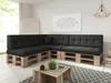 A modern living room with a sectional sofa made of pallets and black cushions, a coffee table made of wooden crates, and a geometric wall art. Produktbild-Vorschau