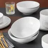 A collection of white ceramic bowls and a glass of water are arranged on a table. Náhled obrázku produktu