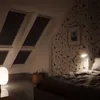 A bedroom scene with a bed, a lamp, and a basket, with skylights in the background. Produktbild-Vorschau