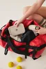 A person is packing a red duffel bag with various items, including a water bottle and a lunchbox. Tennis balls are scattered around the bag. Produktbild-Vorschau
