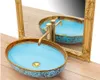 A decorative washbasin with a gold faucet and ornate gold trim, placed on a wooden surface with a gold-framed mirror reflecting the basin. Náhľad obrázku produktu