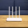 A white router with four antennas sits on a wooden table in front of a blue upholstered surface. Podgląd zdjęcia produktu