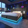 A modern bedroom with a technologically themed decor, featuring a bed with LED lighting, a desk with multiple computer monitors, and abstract geometric wall art with blue neon accents. Produktbild-Vorschau