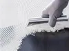 A gloved hand uses a trowel to spread white adhesive onto a dark surface, creating a textured pattern. Produktbild-Vorschau