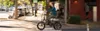 A man rides a folding electric bicycle down a street lined with trees and buildings. Anteprima dell’immagine prodotto
