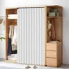 A white pleated curtain hangs in front of a wooden wardrobe, partially obscuring the clothes inside. The wardrobe has shelves and drawers, with some items like hats and boxes visible. Náhled obrázku produktu