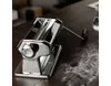 A chrome pasta maker rests on a wooden table with flour scattered around it. Náhled obrázku produktu