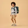 A young boy wearing a backpack stands against a plain background. Produktbild-Vorschau