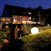 A garden ball light illuminates a grassy area in front of a building at dusk. Anteprima dell’immagine prodotto