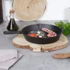 A cast iron pan with ingredients for cooking is placed on a wooden board on a kitchen counter. Náhled obrázku produktu