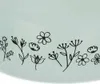A close-up view of a light blue surface with a decorative border of black line-drawn flowers and leaves. Voir les images du produit