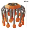 An orange and grey octopus-like head massager sits on a white background with a measurement indicator. Produktbild-Vorschau