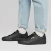 A person wearing black Puma shoes and light blue jeans. Podgląd zdjęcia produktu