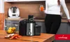 A juicer is shown on a wooden table in a kitchen setting. A person is holding a glass of juice in the background. Produktbild-Vorschau