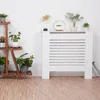 A white radiator cover is shown in a room with a wooden floor and a white wall. There are plants on a wooden shelf to the left and decorative items on top of the radiator cover. Anteprima dell’immagine prodotto