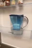 A blue water filter pitcher sits on a shelf in a refrigerator. Náhled obrázku produktu