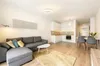 A modern living room and kitchen area with a sofa, coffee table, rug, and dining set. Produktbild-Vorschau
