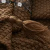 A close-up of a brown knitted blanket with a tassel. Anteprima dell’immagine prodotto