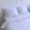 A white duvet cover and pillow set with ruffled edges on a bed. Podgląd zdjęcia produktu