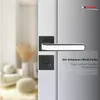 A close-up of a black and white door handle set on a door, with a blurred background of a room interior. Produktbild-Vorschau