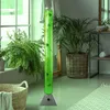 A tall, green LED water column with decorative fish is placed in a room with plants and a basket. Produktbild-Vorschau