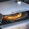 A pizza is being cooked on a grill using a pizza attachment. Podgląd zdjęcia produktu