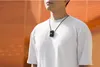 A person wearing a white t-shirt and a black DJI Mic 2 transmitter necklace against an orange and light gray background. Náhled obrázku produktu
