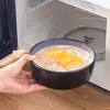 Eine gefüllte Schale wird vor die geöffnete Mikrowelle gehalten. Voir les images du produit