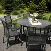 A round outdoor dining table with chairs set up on a paved patio, surrounded by greenery. Produktbild-Vorschau