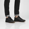 A person wearing black jeans and black Puma sneakers. Voir les images du produit