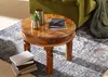 A round wooden coffee table with books, a plant, and a notebook on it, placed on a rug next to a green sofa. Produktbild-Vorschau