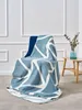 A blue and white geometric patterned blanket draped over a chair in a room with white paneled walls and a small wooden side table with a vase of greenery. Anteprima dell’immagine prodotto