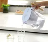 A hand pours filtered water from a pitcher into a glass on a white countertop. Produktbild-Vorschau