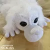 A close-up view of a white crocheted stuffed toy animal with large black eyes and fluffy white fur. Podgląd zdjęcia produktu