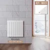 A white panel radiator mounted on a gray tiled wall, with a doorway and balcony visible in the background. Podgląd zdjęcia produktu