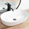 A white oval countertop sink with a black faucet is shown on a wooden surface. Anteprima dell’immagine prodotto