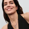 A woman wearing a black top and a silver necklace with a charm. Anteprima dell’immagine prodotto