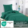 A neatly folded duvet and pillow in a dark green color, displayed on a bed. The background shows a room interior with a vase of flowers and a window. Produktbild-Vorschau