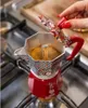 A person is using a decorative Moka pot on a stovetop. Produktbild-Vorschau